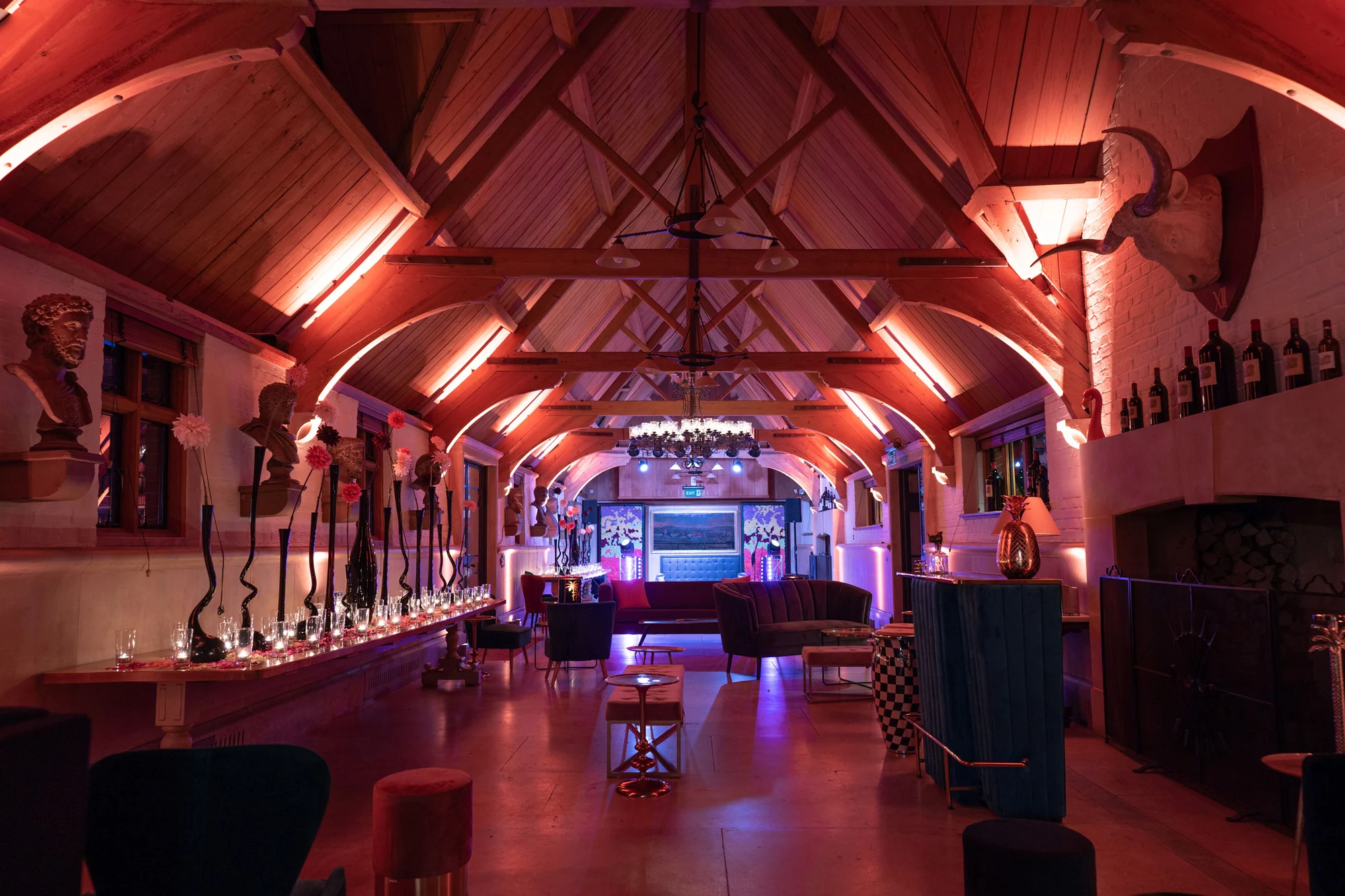 A long space under a timber roof lit deep pink and red, low furniture down one side and a dance floor at the far end.