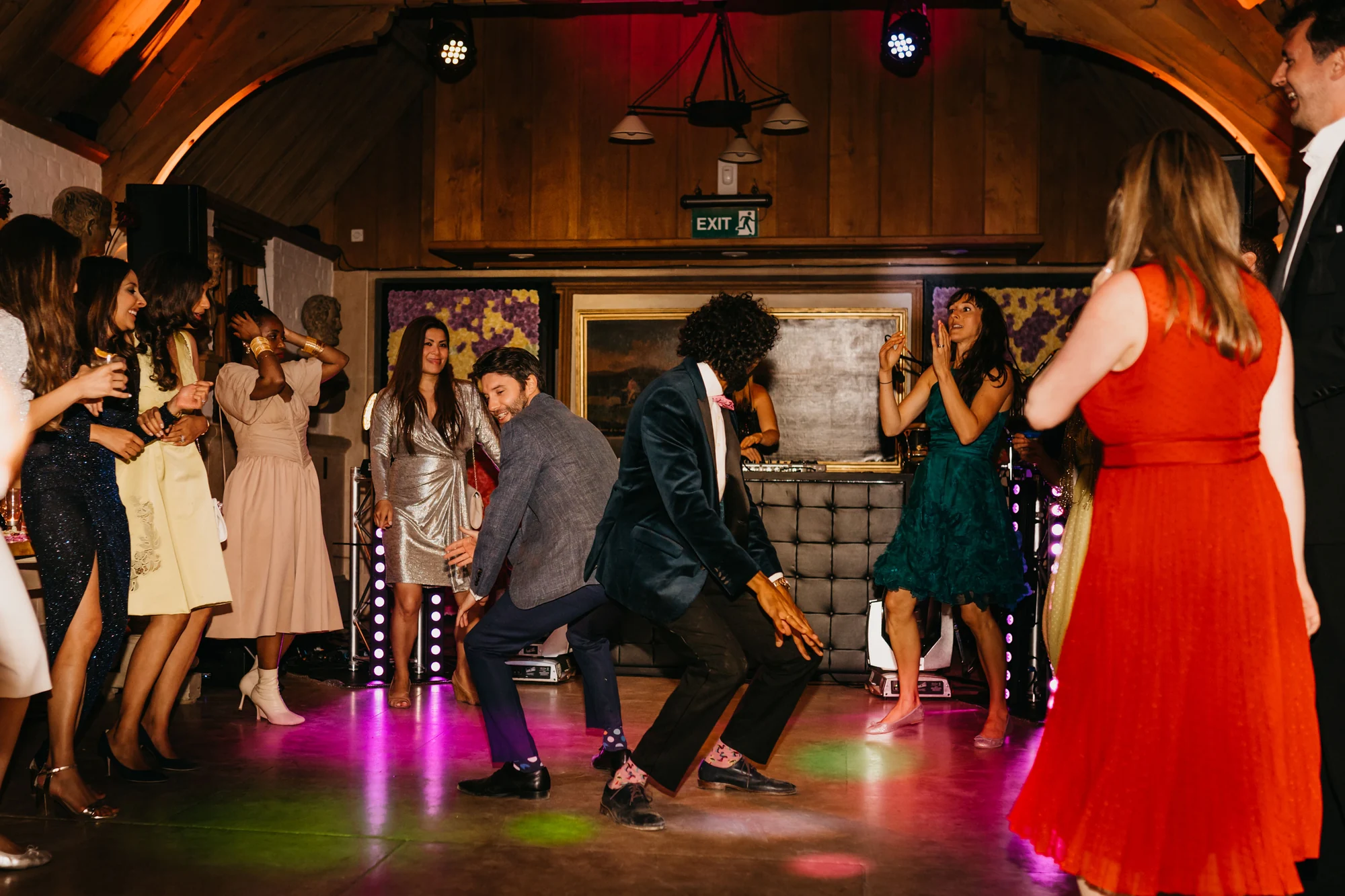 Guests dancing under coloured light, a woman in red at the centre of the floor.
