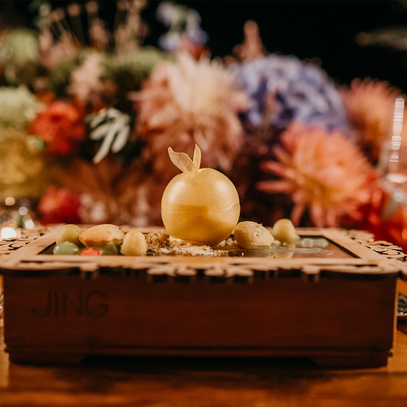 A golden apple filled with brulee cream set on a wooden board among dried flowers and blown glass.