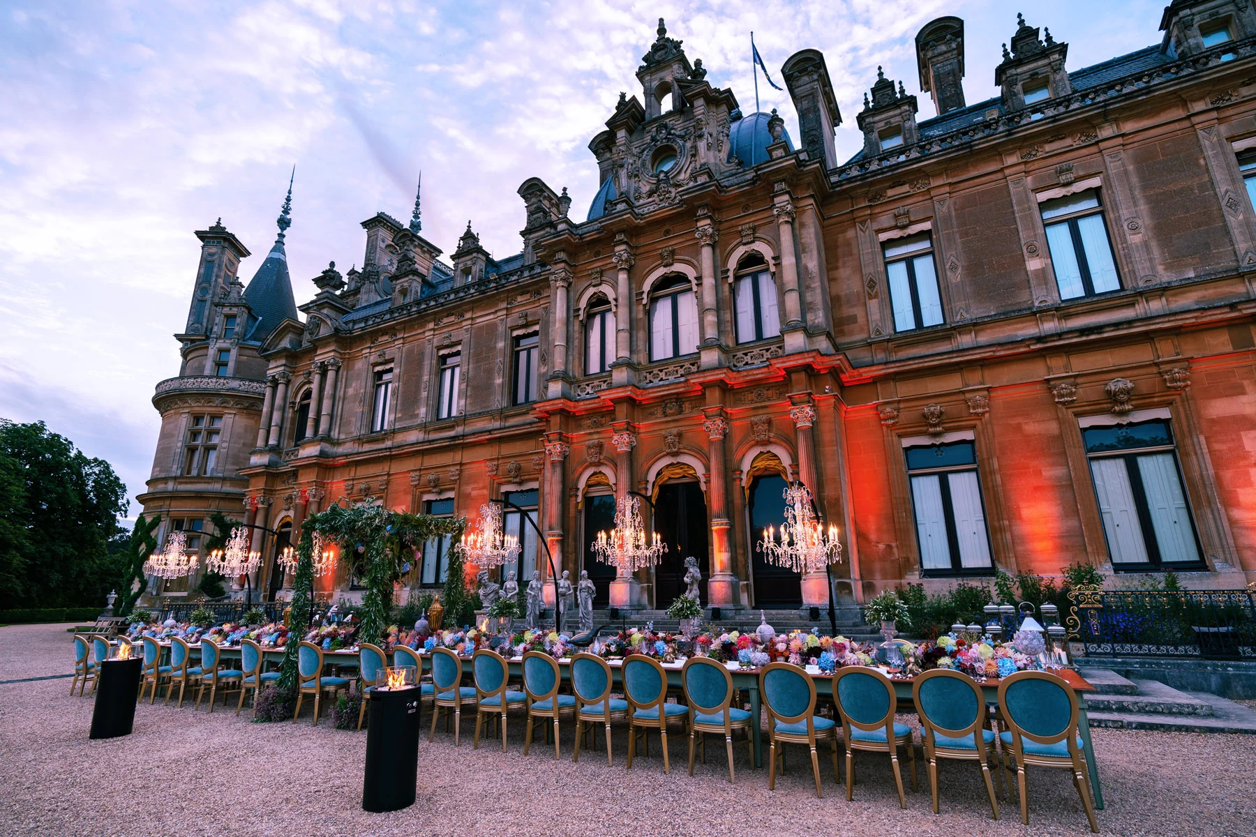 The full length of the laid table running down the Parterre at dusk, blue chairs either side and the manor uplit behind.