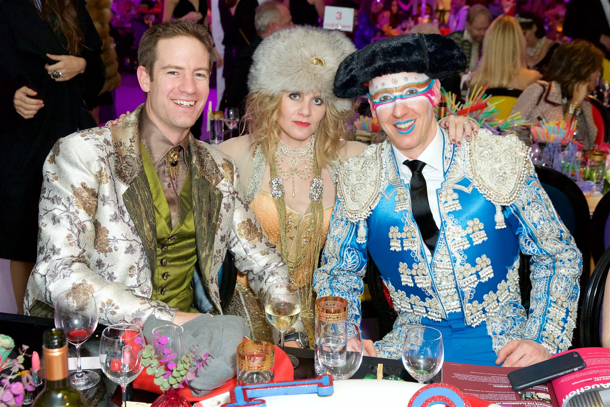 Three guests in silver and blue brocade seated together at the table.