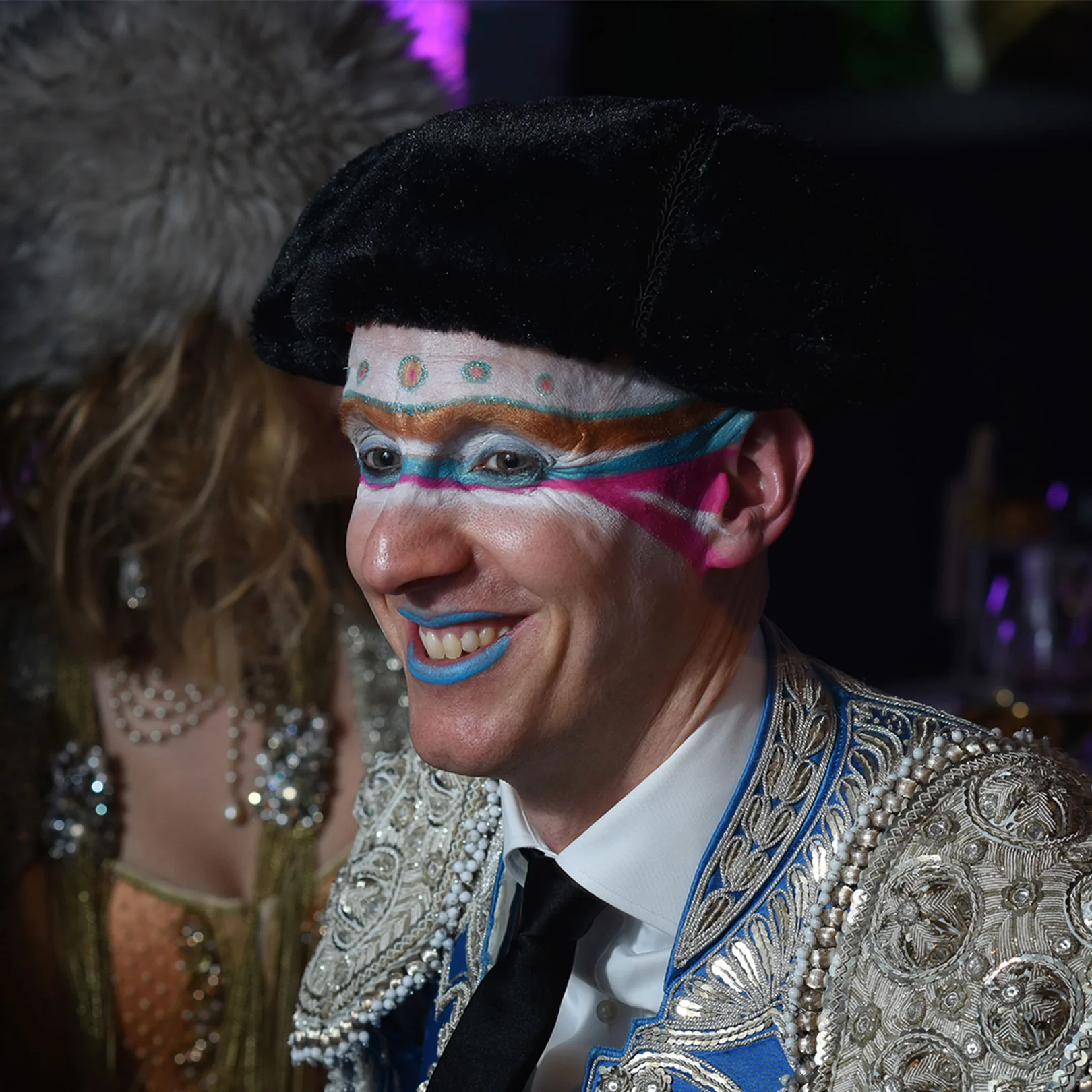 A guest in a silver matador jacket with a painted face and a black hat.