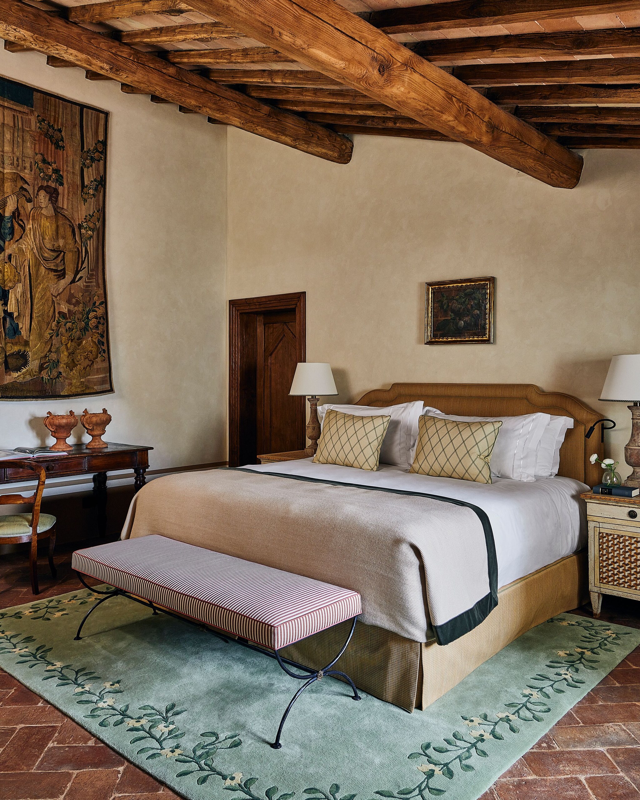 A suite bedroom with tapestry and beamed ceiling at Castello di Casole.