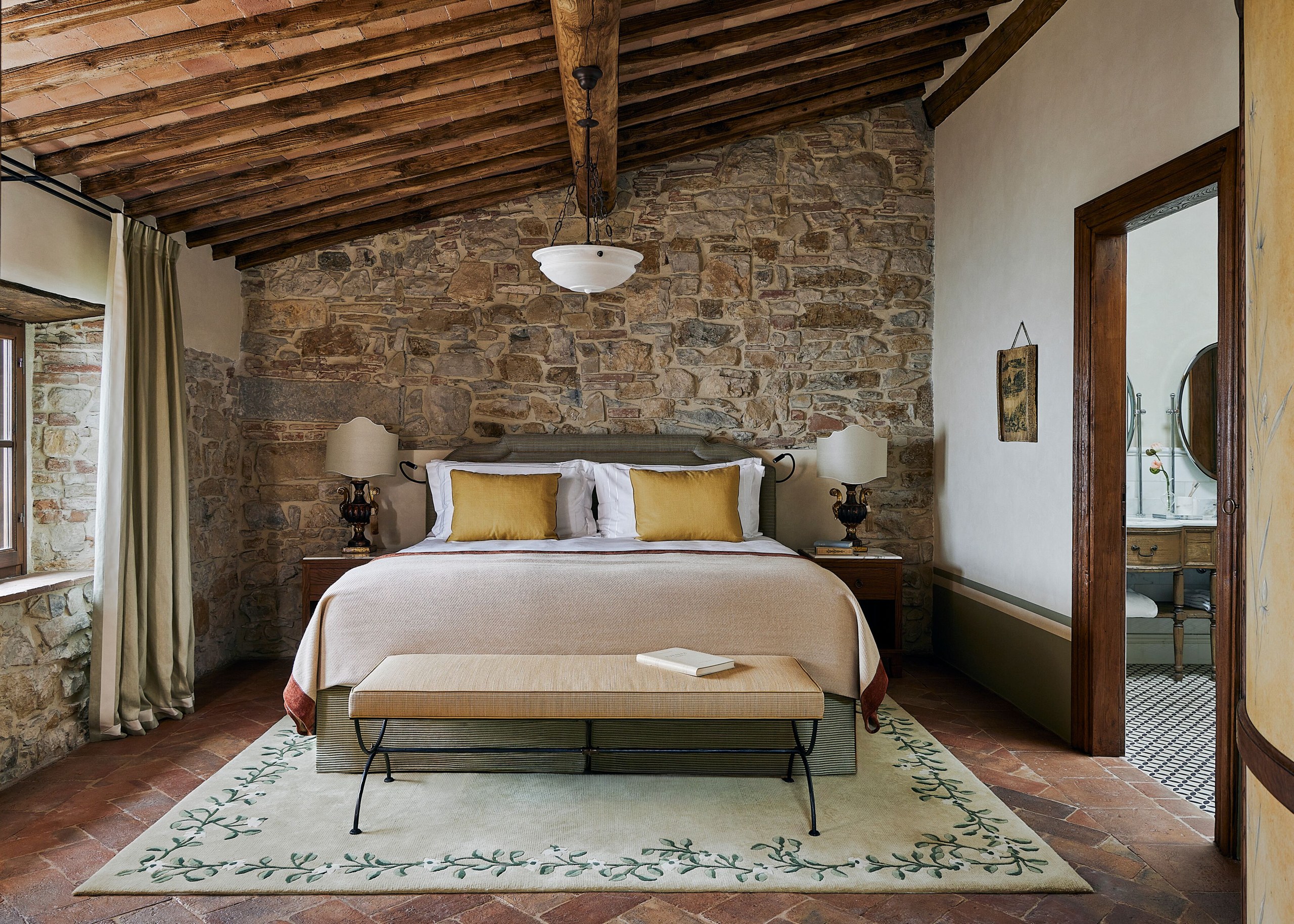 A suite bedroom with stone walls and a beamed ceiling at Castello di Casole.