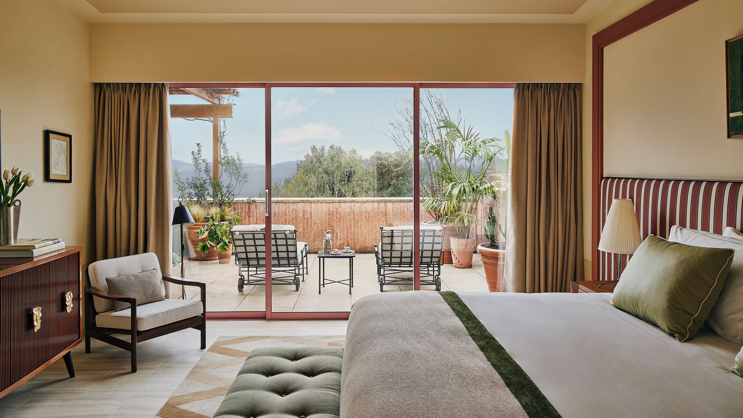 A suite bedroom opening onto a terrace above the Tuscan landscape at Castello di Casole.