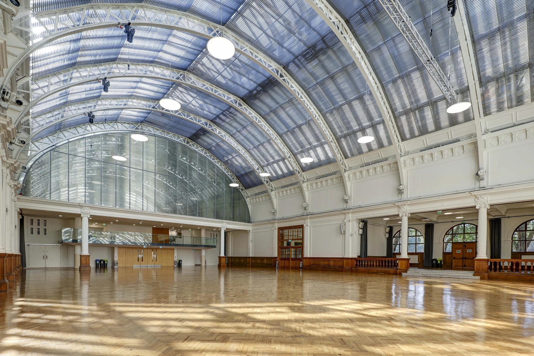 The Main Hall of Lindley Hall from the far end, sunlight across the parquet, the glass vault overhead and the arcades and doors along the side.