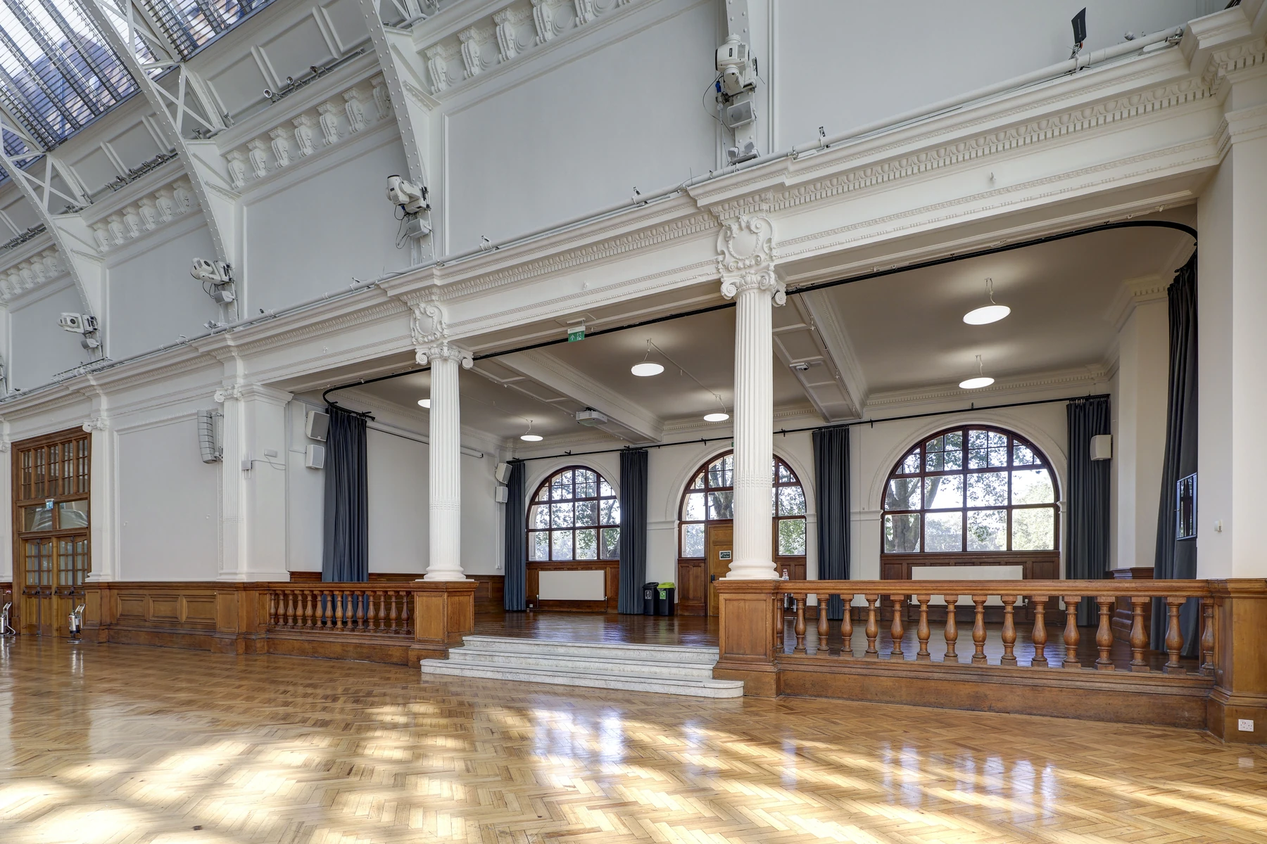 The North Annexe seen from the Main Hall, open to it through white columns, a carved wooden balustrade and steps, arched windows at the back.