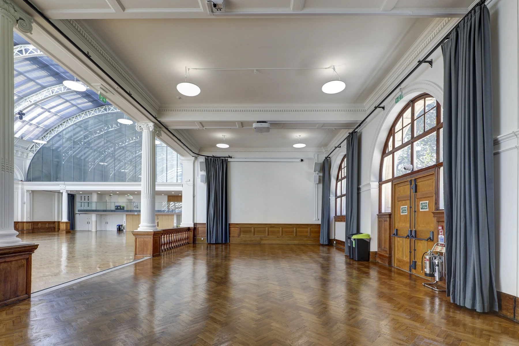 Inside the North Annexe at Lindley Hall, parquet floor, grey curtains and arched windows, the vault of the Main Hall visible through the columns.