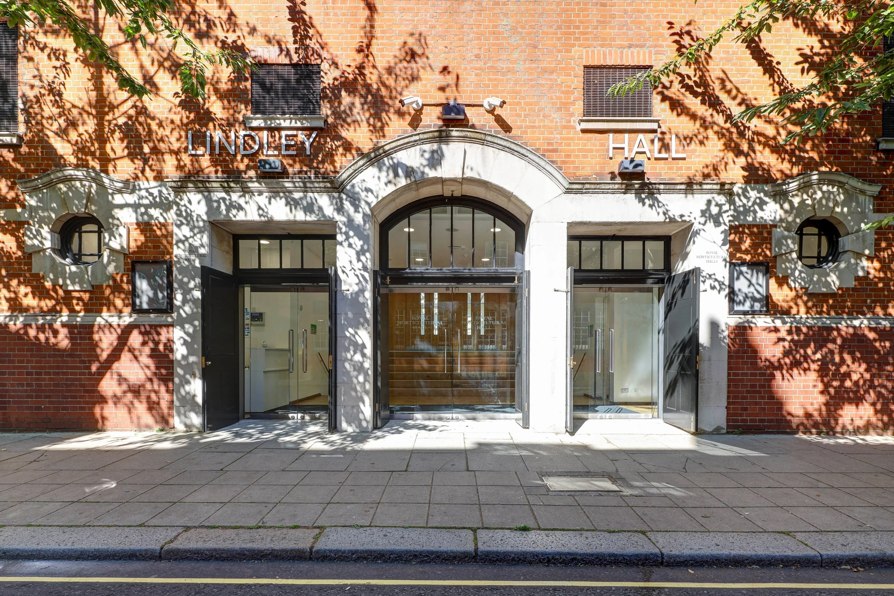 The front of Lindley Hall in red brick and white stone, the name in metal letters above three doorways, the central one arched, trees overhead.