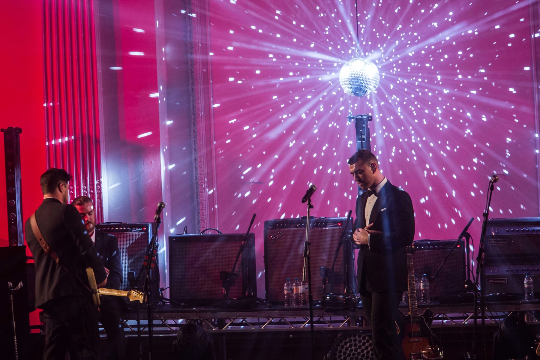 A mirror ball on the truss above the stage throwing white light across a pink wall, two musicians below it.