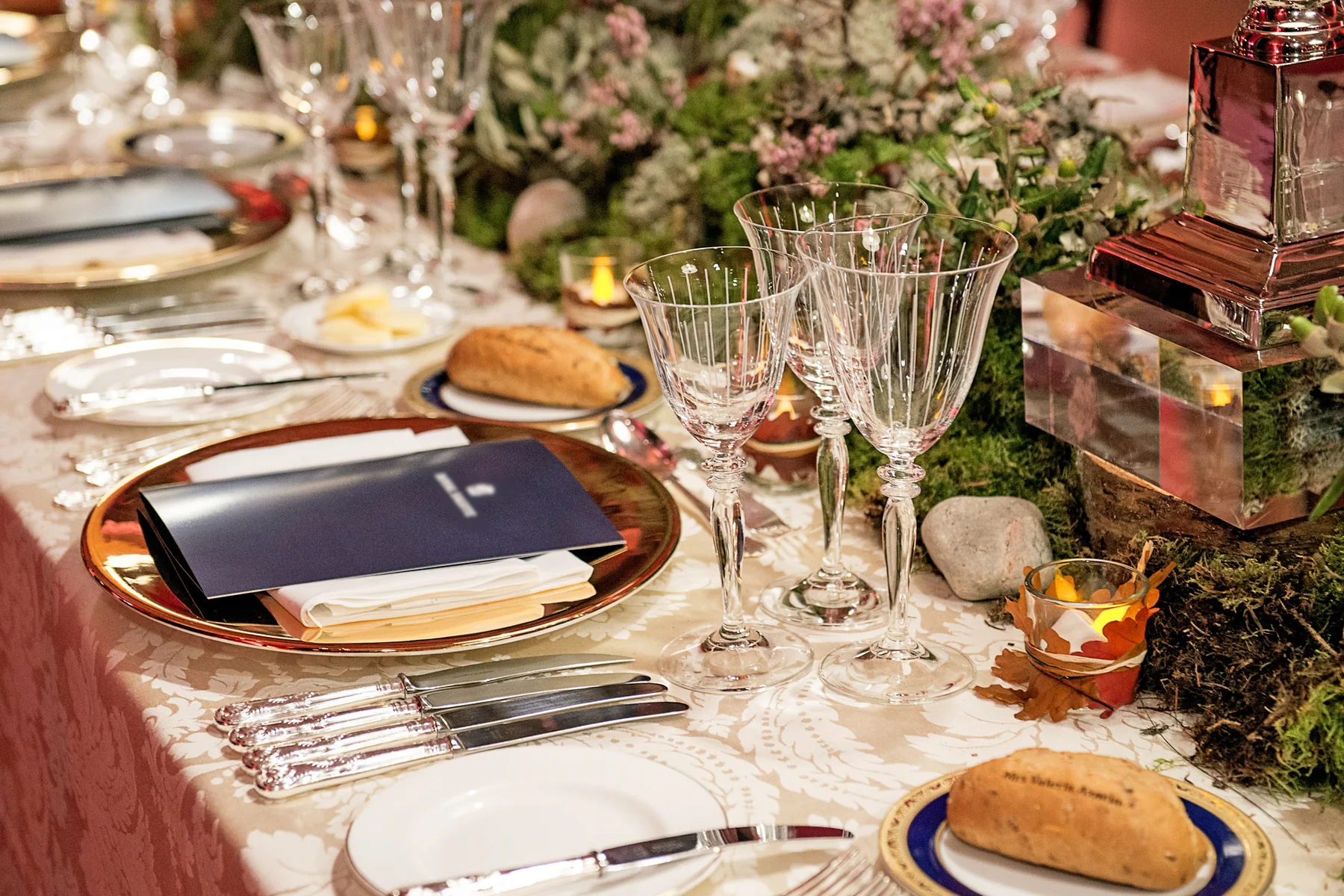 A place setting with the barley bread roll, moss and pebbles along the table.