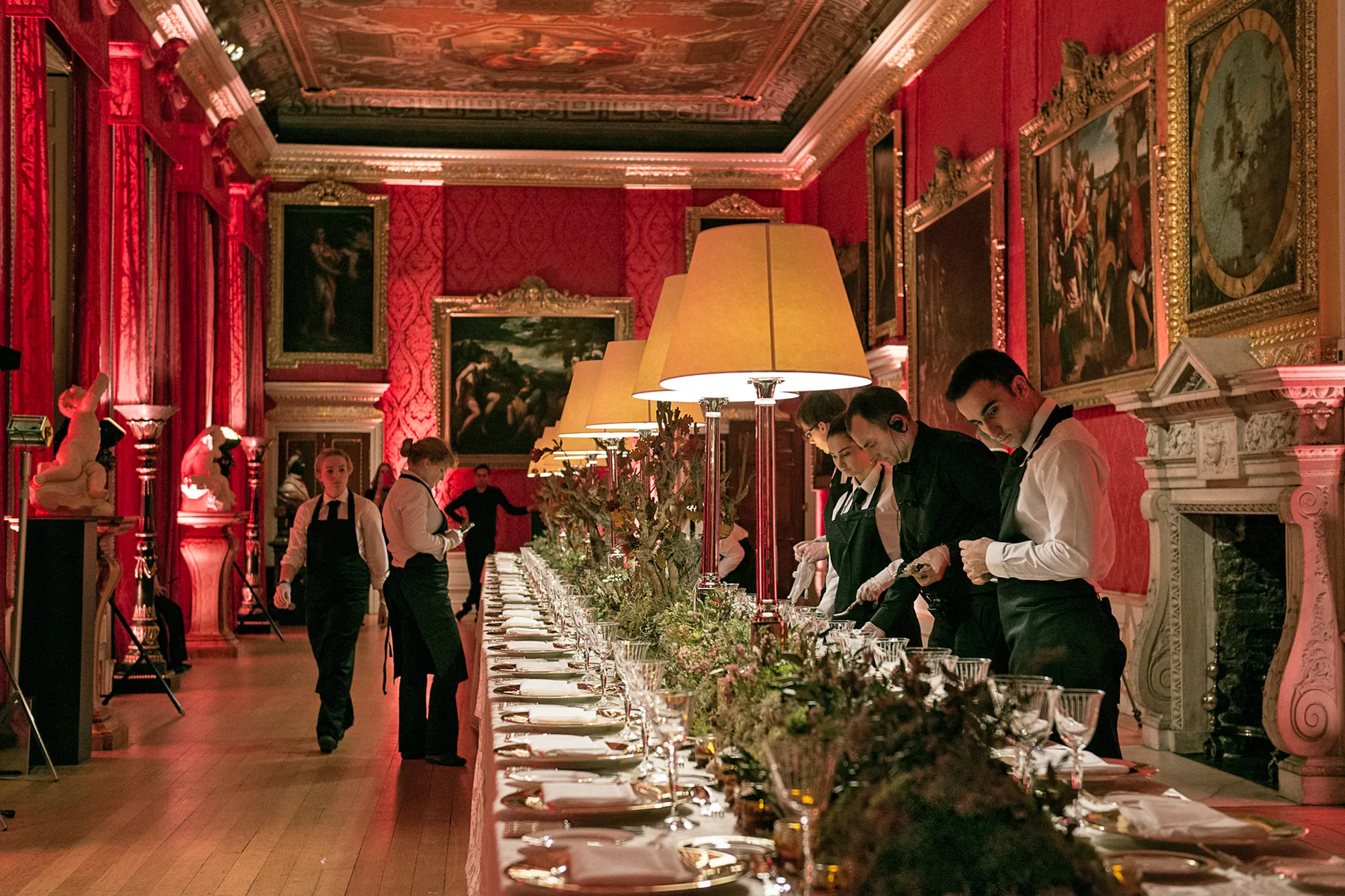 The full length of the laid table beneath the red damask and the hung paintings.
