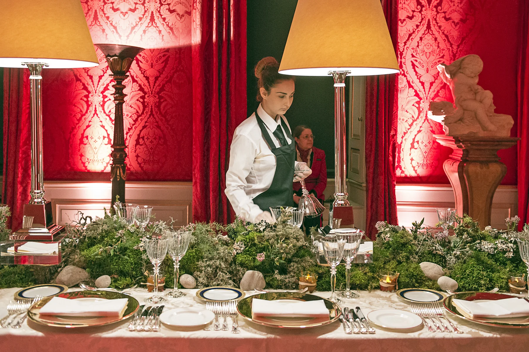 The table with staff standing behind it, the shaded lamps lit along its length.