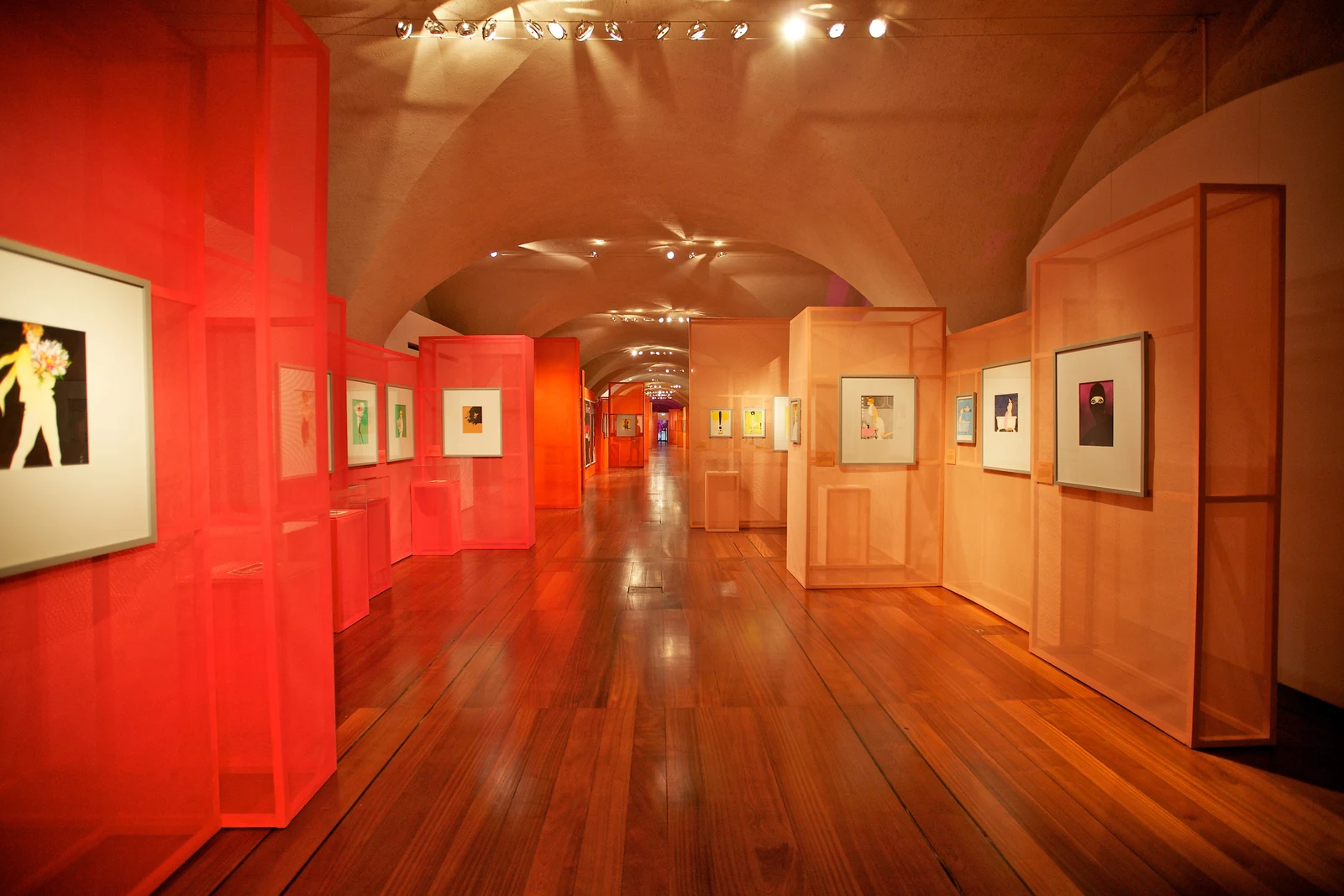 Framed fashion illustrations hung inside translucent orange panels running down the length of the vault, the wooden floor reflecting the light.