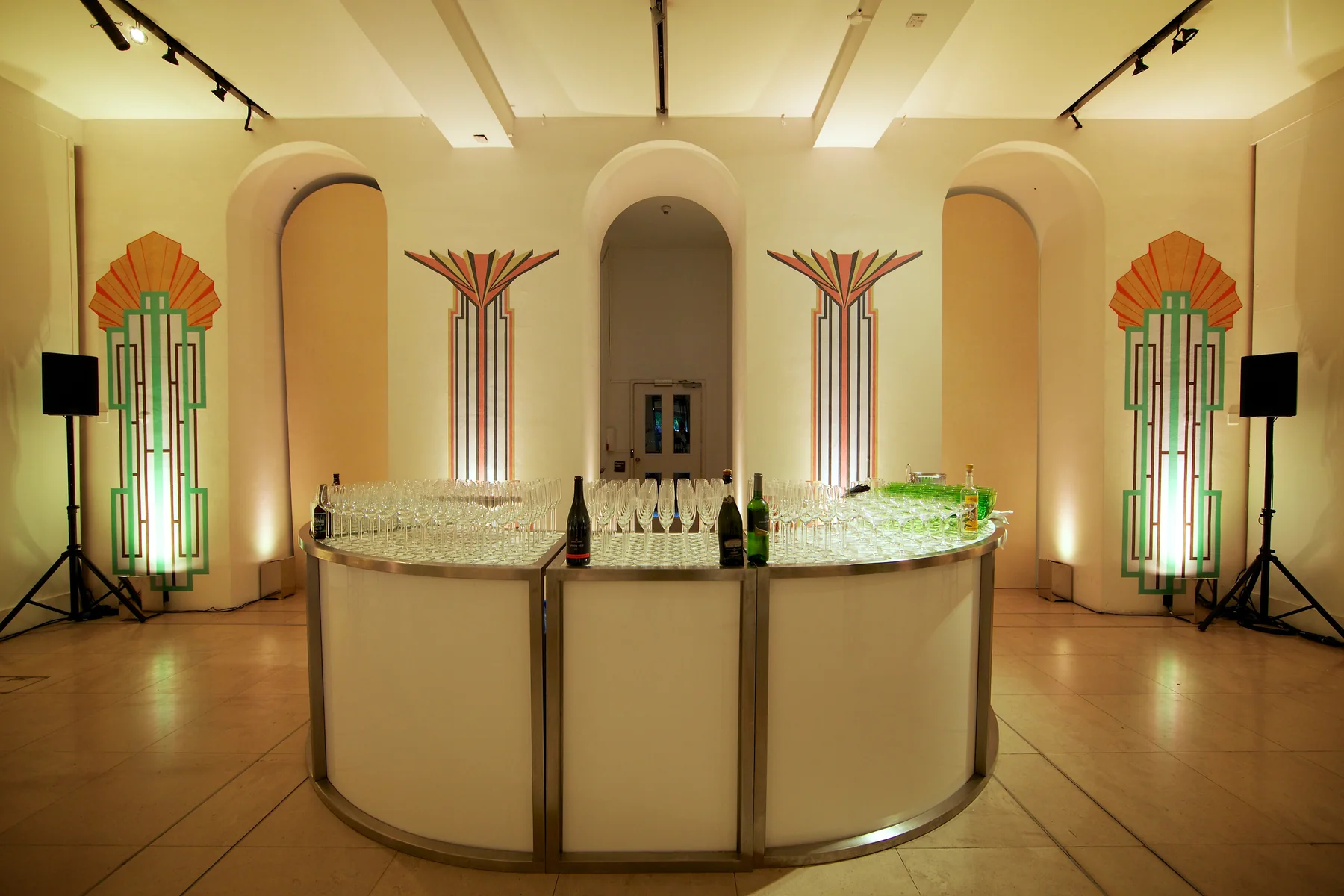 The finished curved bar, glassware set out, the Deco column artwork mounted behind it.