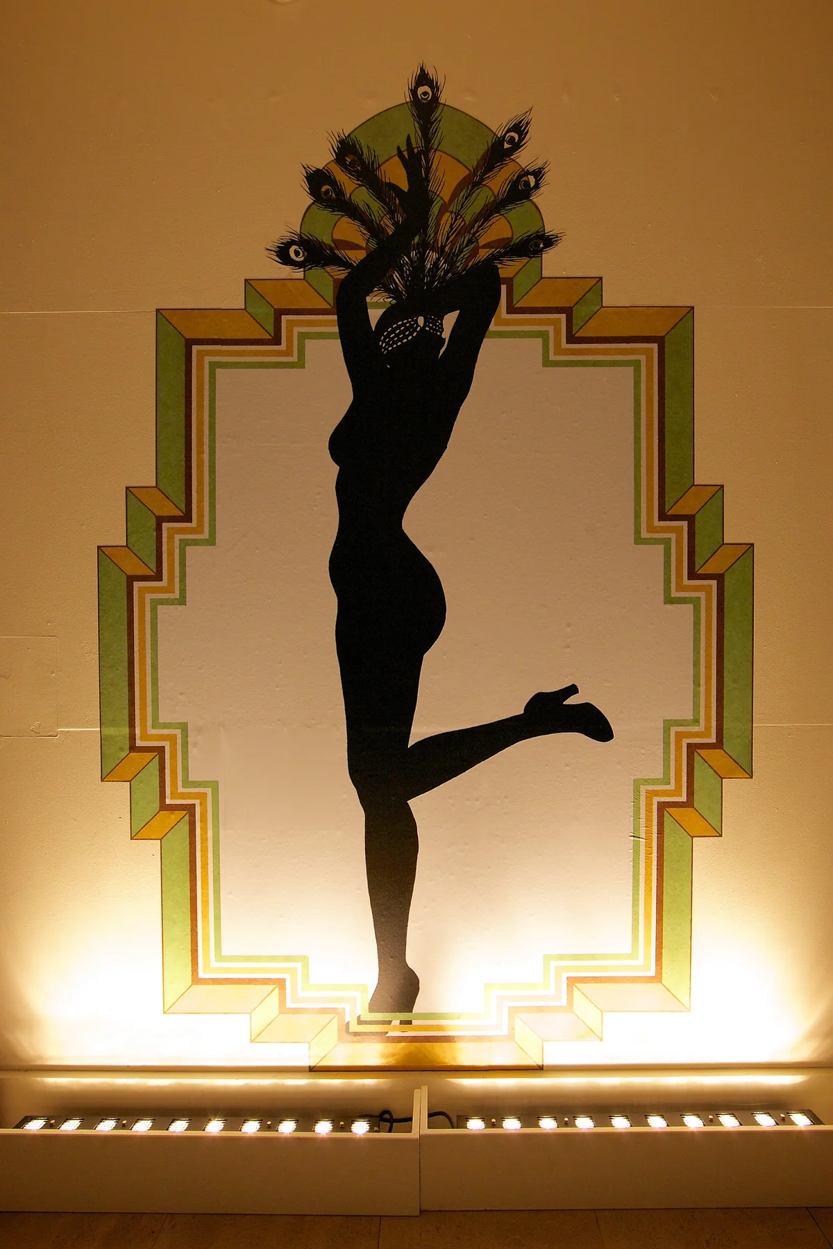 A cabaret dancer in silhouette, one leg kicked high, inside a stepped Art Deco frame.