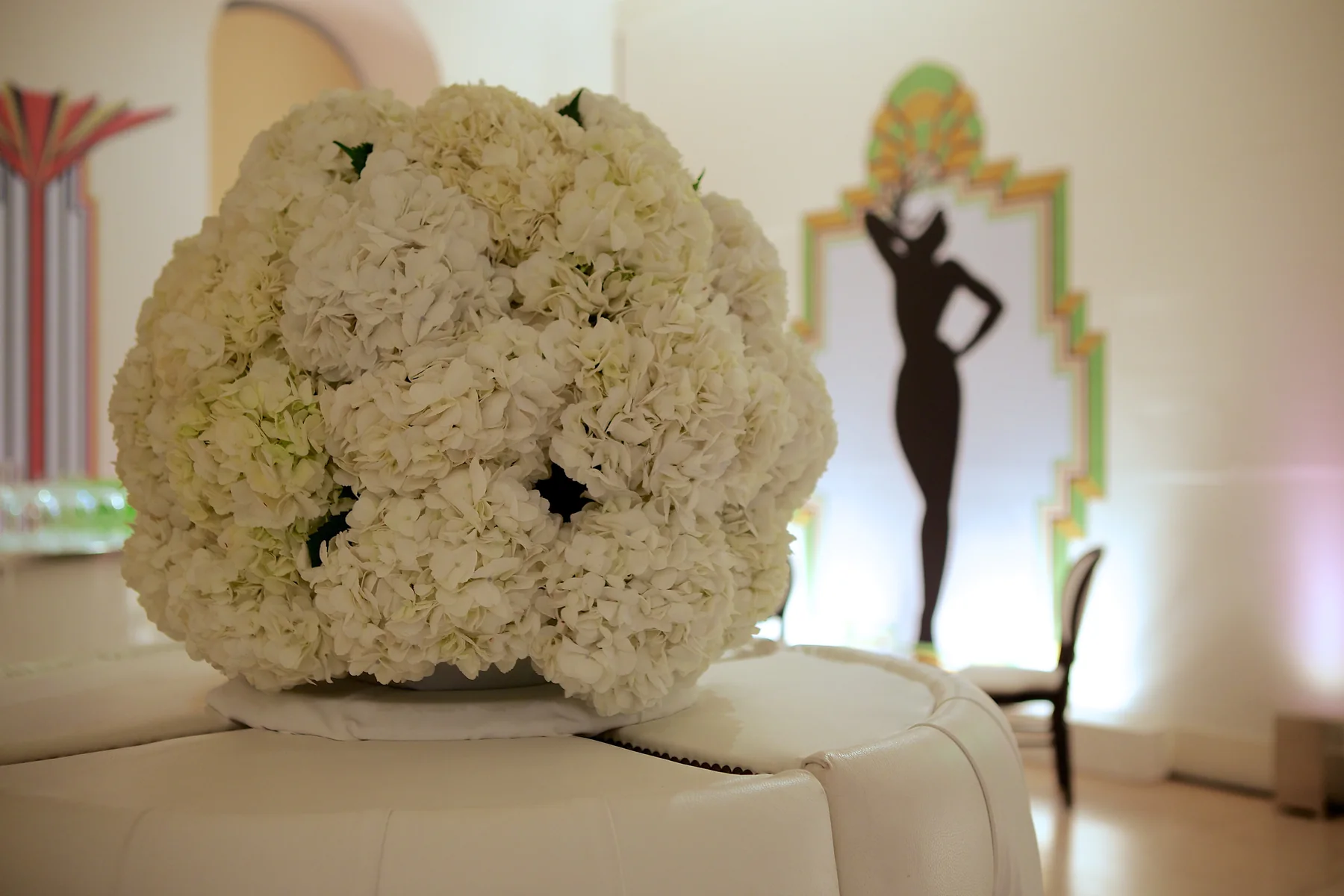 A white hydrangea ball on the banquette, a dancer panel lit behind it.