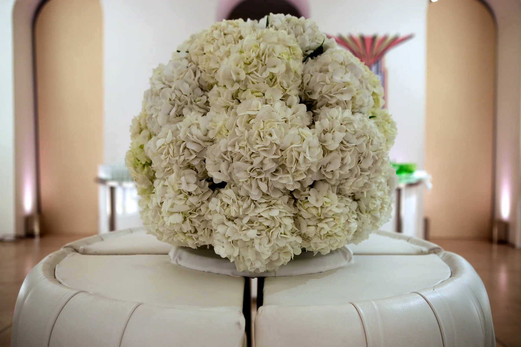 The hydrangea ball seen wider, the cream banquette curving away beneath it.