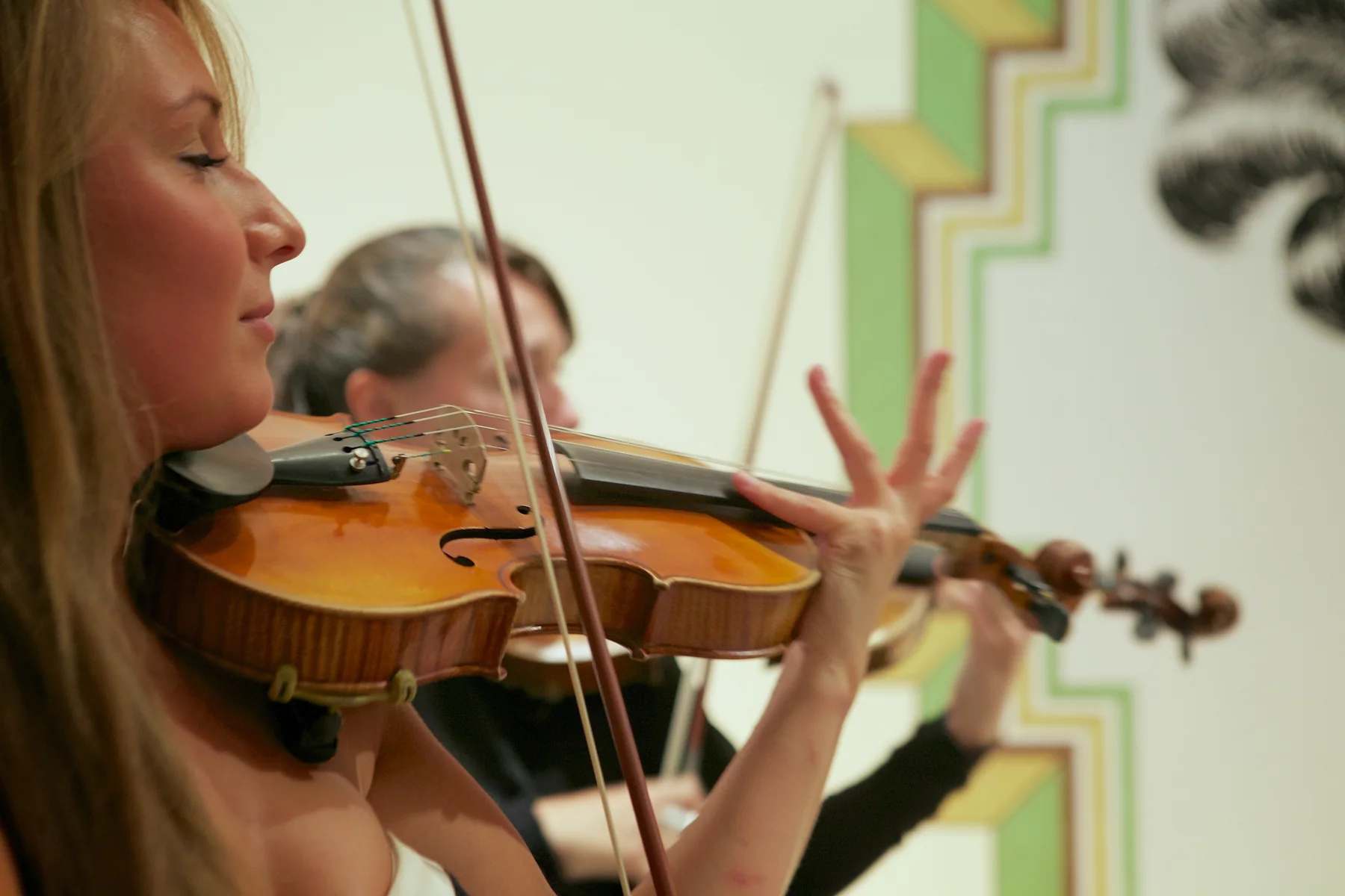 A violinist of the string quartet playing, the Deco artwork behind her.
